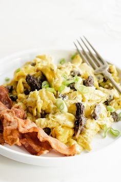 a white plate topped with eggs, bacon and green onions next to a knife and fork