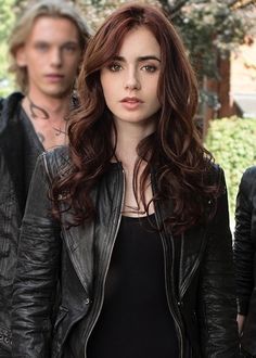 a woman with long hair standing in front of another man wearing black leather jacket and jeans