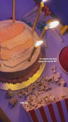 a birthday cake sitting on top of a table next to some popcorn and two lit candles