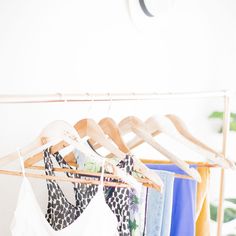 clothes hanging on wooden hangers in front of a white wall and potted plant