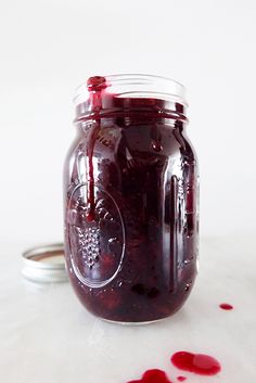 a jar filled with red liquid sitting on top of a white table next to a spoon