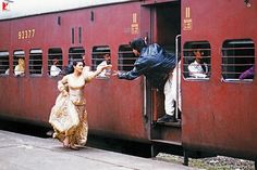 a woman in a long dress standing on the side of a train as people board it