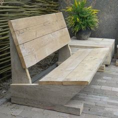 a wooden bench sitting on top of a brick floor next to a potted plant