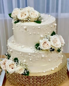 a three tiered wedding cake with white flowers and pearls on the top, sitting on a table