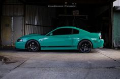 a green mustang car parked in front of a garage with the door open and it's hood up