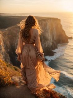 a woman standing on top of a cliff next to the ocean with her back to the camera