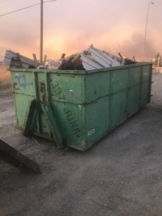 a green dumpster sitting on top of a dirt field