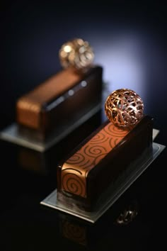 two gold rings sitting on top of a chocolate cake with an intricate design and brown icing