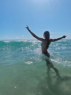 a woman standing in the ocean with her arms outstretched