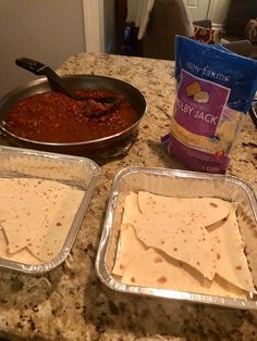 three pans filled with food sitting on top of a counter next to a bag of chips