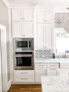 a kitchen with white cabinets and stainless steel appliances in the center, along with a marble counter top