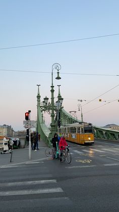 people are crossing the street in front of a yellow bus and green traffic light on a sunny day