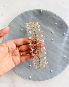 a hand holding a piece of jewelry on top of a plate with pearls and leaves