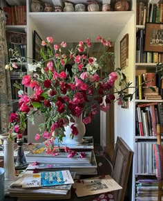 a vase filled with pink flowers sitting on top of a wooden table next to books