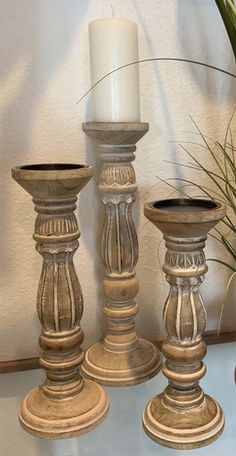 three tall candlesticks sitting on top of a table next to a potted plant