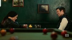 a man and woman sitting at a pool table in a bar talking to each other