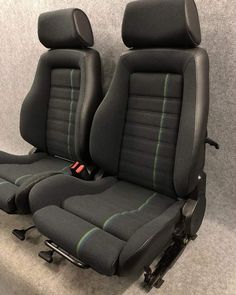 two black seats with green stitching sit in front of a gray wall and grey carpet