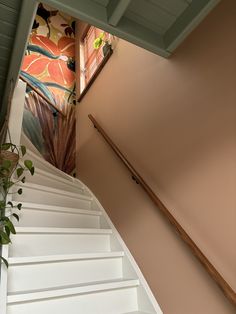 a stair case next to a plant on top of a wooden hand rail in front of a painted wall