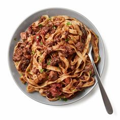 a bowl filled with pasta and meat on top of a white table next to a fork