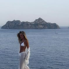 a woman standing on top of a rock next to the ocean with an island in the background