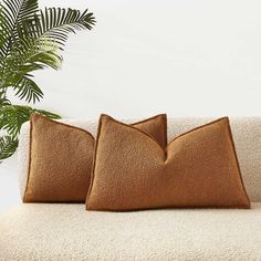 two brown pillows sitting on top of a couch next to a potted palm tree