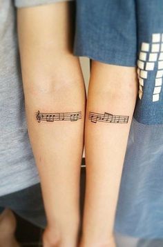 two people with matching tattoos that have musical notes tattooed on their arms, both of them are holding hands