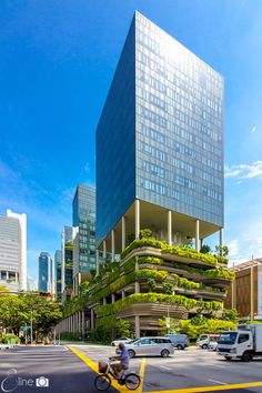 a person riding a bike on the street in front of a tall building with plants growing on it