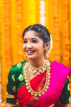 a woman in a red and green sari smiles at the camera while wearing gold jewelry