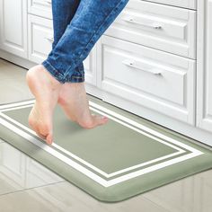 a woman standing on top of a kitchen floor next to a green mat with white stripes