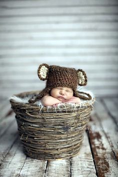 a newborn baby wearing a brown bear hat in a wicker basket on a wooden floor