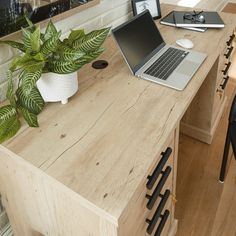 a laptop computer sitting on top of a wooden desk next to a potted plant