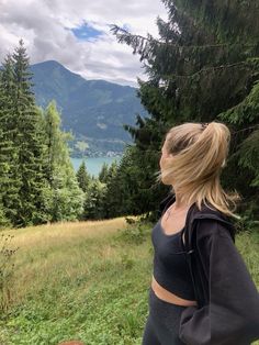 a woman standing on top of a lush green hillside next to a tree filled forest