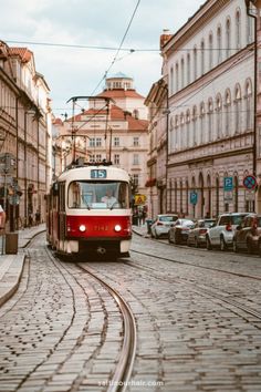 a red and white train traveling down a street next to tall buildings on either side