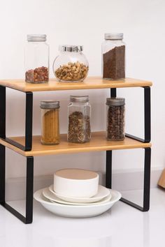 three tiered shelving unit with spice jars and bowls on the top shelf next to a white plate