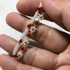 a hand holding a beaded bracelet with red, white and gold beads on it