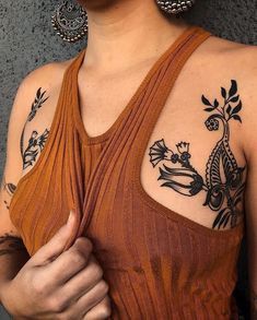 a woman with tattoos on her chest and arm is holding something in her right hand