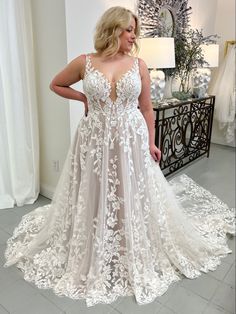 a woman standing in front of a mirror wearing a white wedding dress with floral appliques