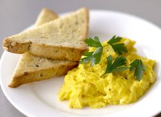 scrambled eggs and toast on a plate with parsley sprig garnish