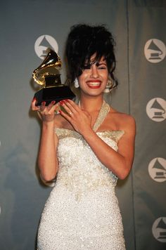 a woman in a white dress holding an award for best performance by a musical group