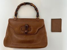 This 70s Gucci Bamboo 1947 small top handle bag, is a vintage treasure crafted in Italy from rich tan brown leather with gold-plated hardware. The iconic bamboo handle gives it a distinctive character.  While pre-owned with visible signs of use, it remains undamaged and in very good condition, offering a sense of history without compromising its functionality or beauty.  The interior is lined with smooth leather, complete with inner pockets for organization.  Included is the original Gucci card 70s Gucci, Gucci Bamboo 1947, Small Top Handle Bag, Treasure Crafts, Gucci Bamboo, 70s Vintage, Handle Bag, Leather Top, Tan Brown