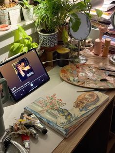 a laptop computer sitting on top of a wooden desk next to potted plants and other items