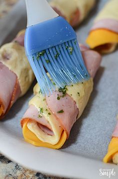 ham and cheese stuffed pastries being brushed with a blue brush on a white plate