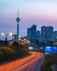 the city skyline is lit up at night with light streaks on the road and buildings in the background