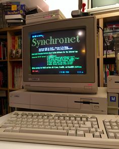 an old computer sitting on top of a desk in front of a book shelf filled with books