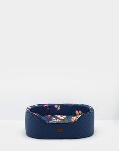 a blue dog bed with floral print on the front and bottom, sitting against a white wall