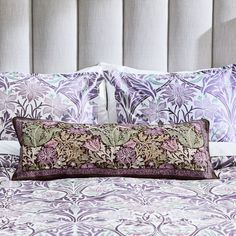 a bed with purple and green pillows on top of it next to a white headboard