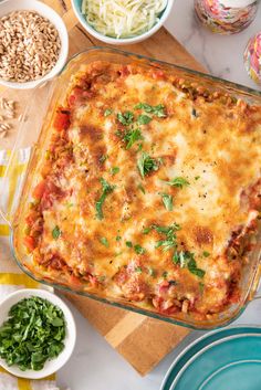 a casserole dish with meat, cheese and vegetables on a table next to other dishes