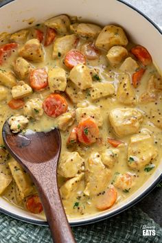 a pan filled with chicken and vegetables next to a wooden spoon