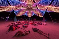 several people laying on the ground in front of an artistic structure with lights all over it