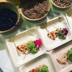 several plates with different types of food on them and bowls full of seeds in the background